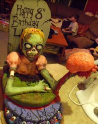 Zombie birth cake with Female zombie coming out from a graveyard holding a brain.JPG