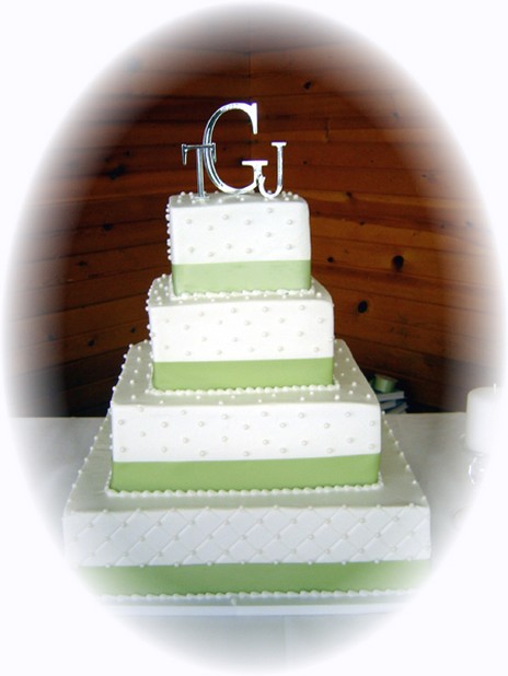 four tier square wedding cake with green ribbons and topper