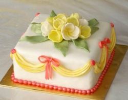 Square white cake with yellow drapes and white and yellow flowers on top.JPG