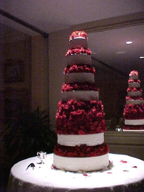 tall wedding cake with red flowers and there are alot of them