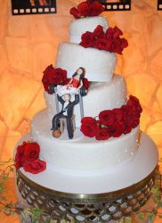 Humorous 4 tier round white wedding cake with red roses and groom bench pressing bride.JPG