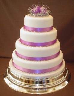 elegant wedding cake with purple ribbons and purple flowers topper